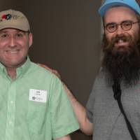two men, both wearing ball caps, pose for photo together